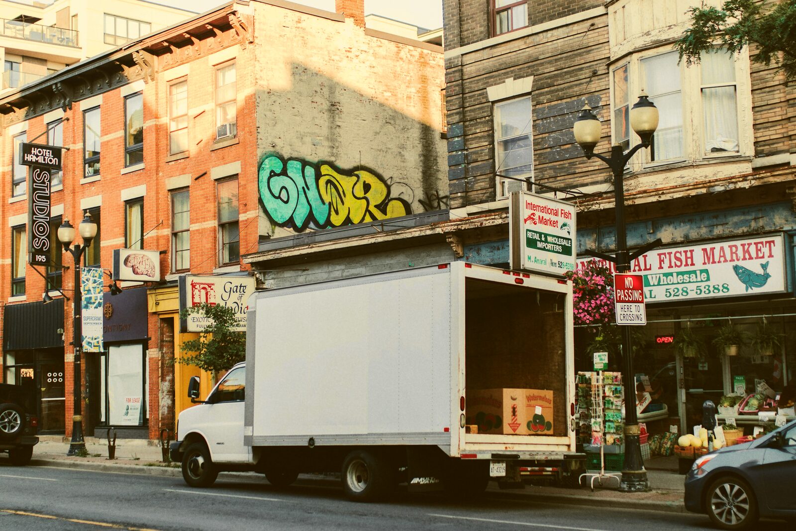 A white delivery box truck parked on a city street beside storefronts.