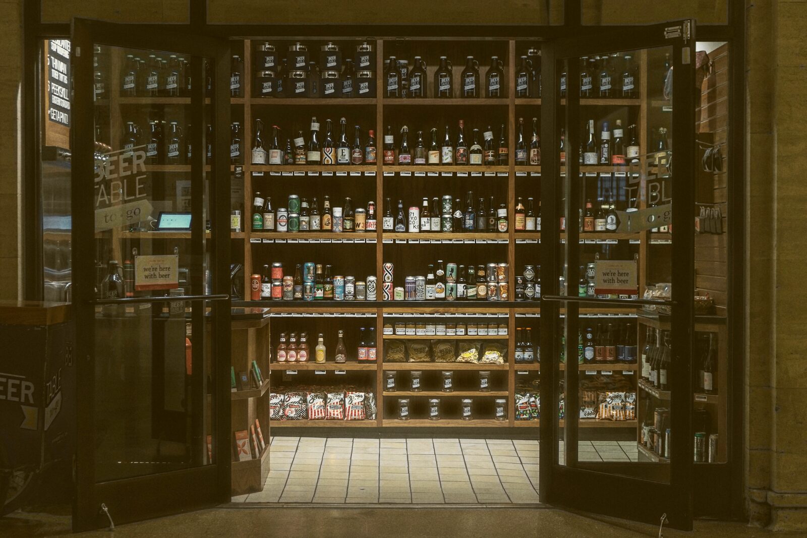 A glass storefront door opens onto shelves stocked with rows of bottled drinks.