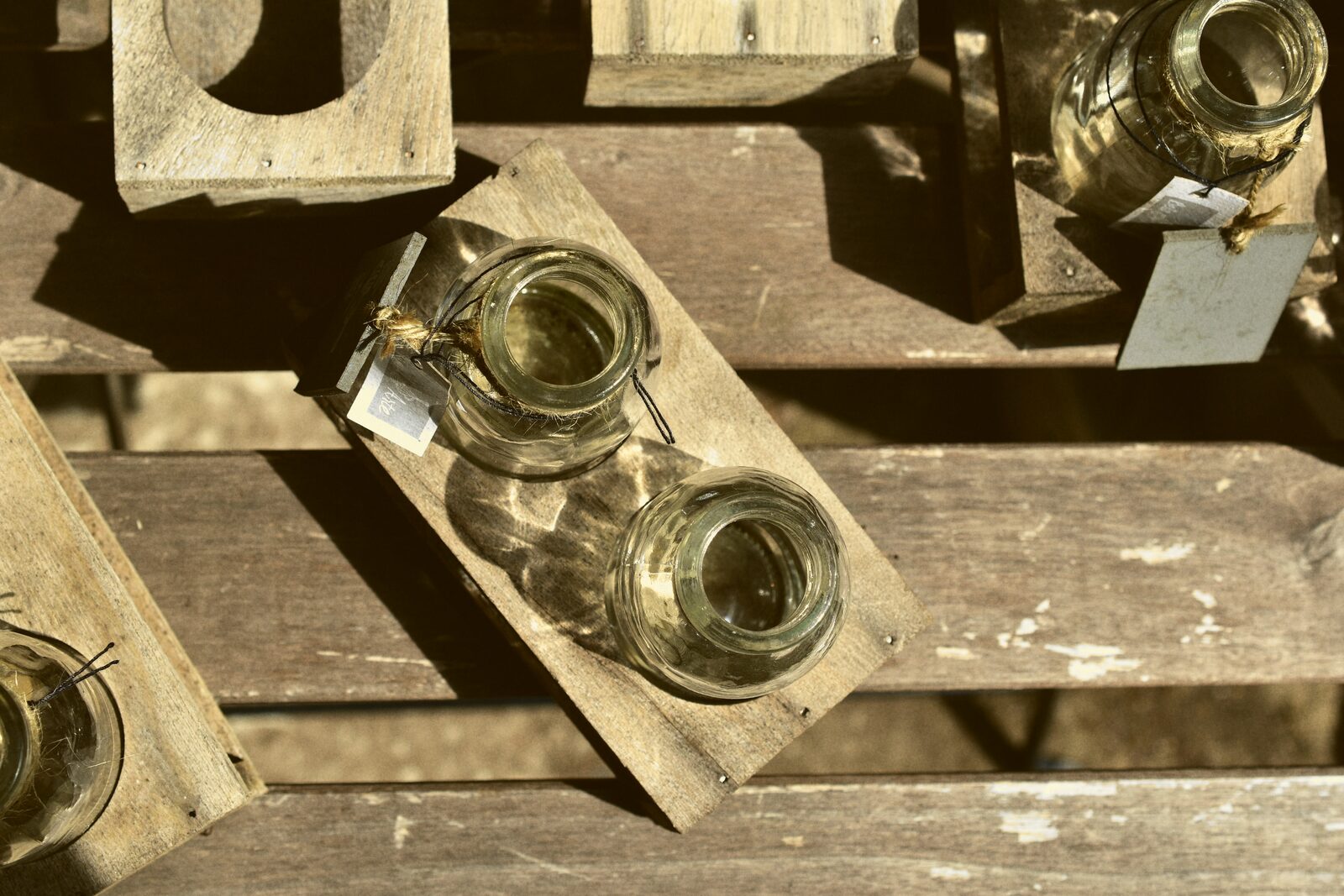 Small glass jars with tied paper tags resting on a wooden crate in sunlight.