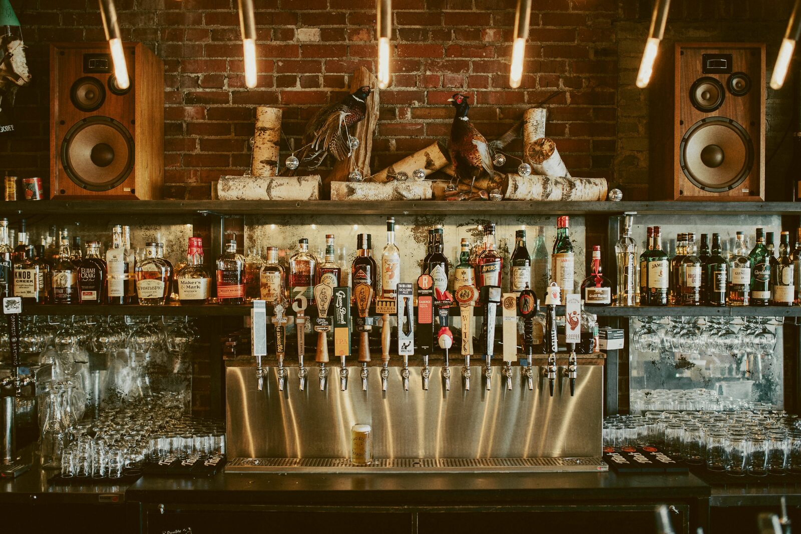 A brick-walled back bar lined with bottles beneath hanging pendant lights.