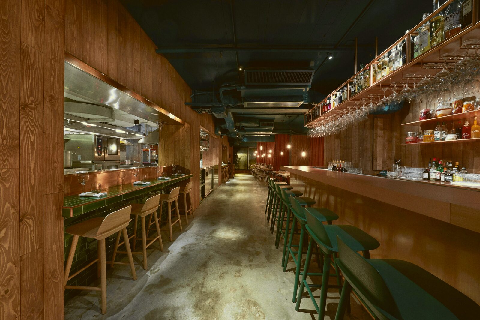 A narrow wood-paneled bar interior with green stools and shelved bottles.
