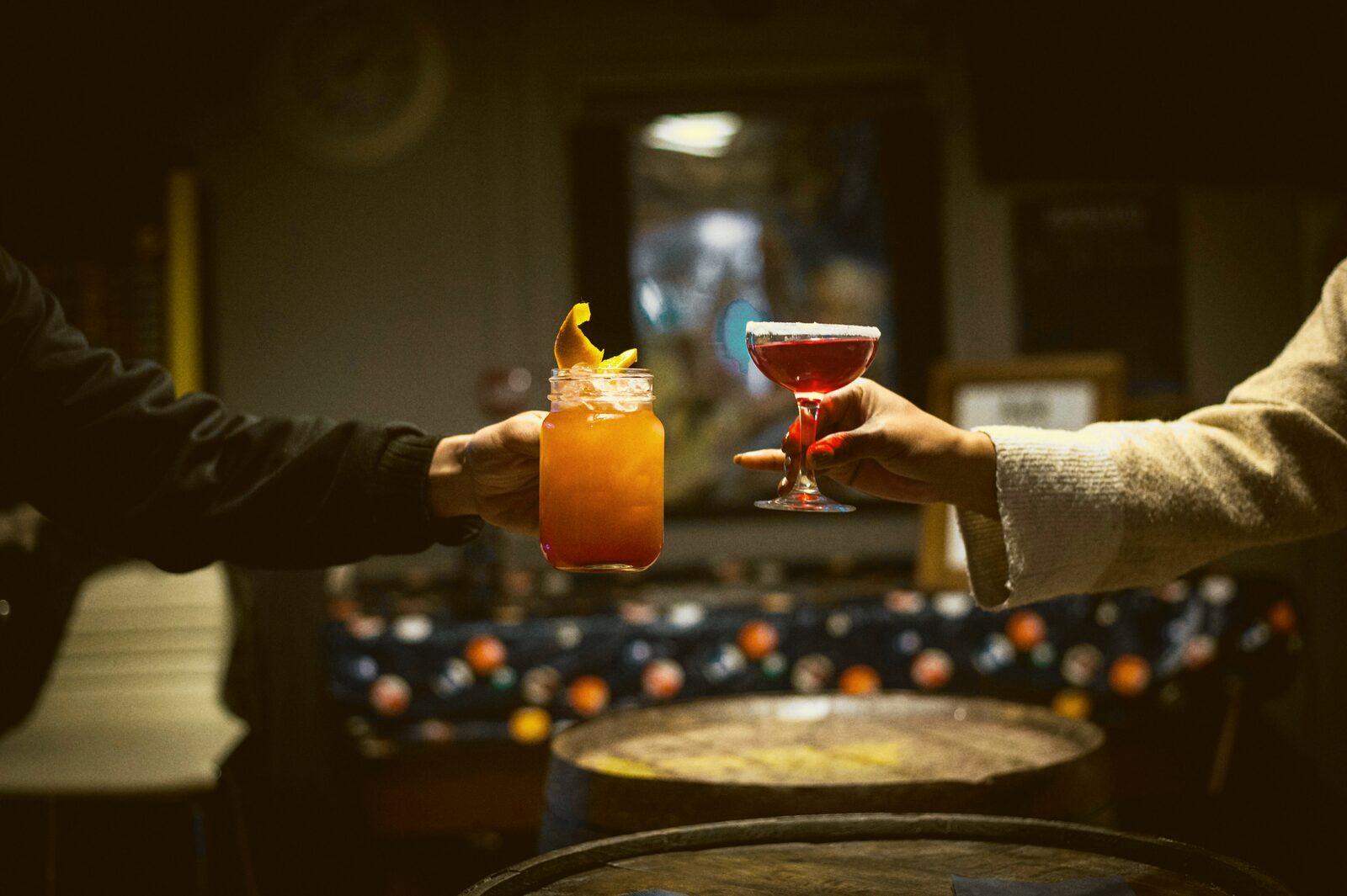 Two hands clink glasses together in a dimly lit room.
