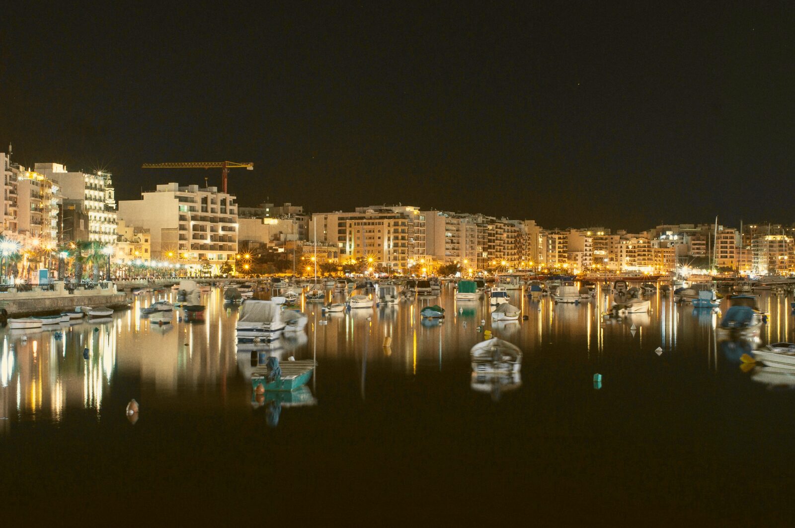 A marina lined with moored boats and waterfront buildings lit up at night.