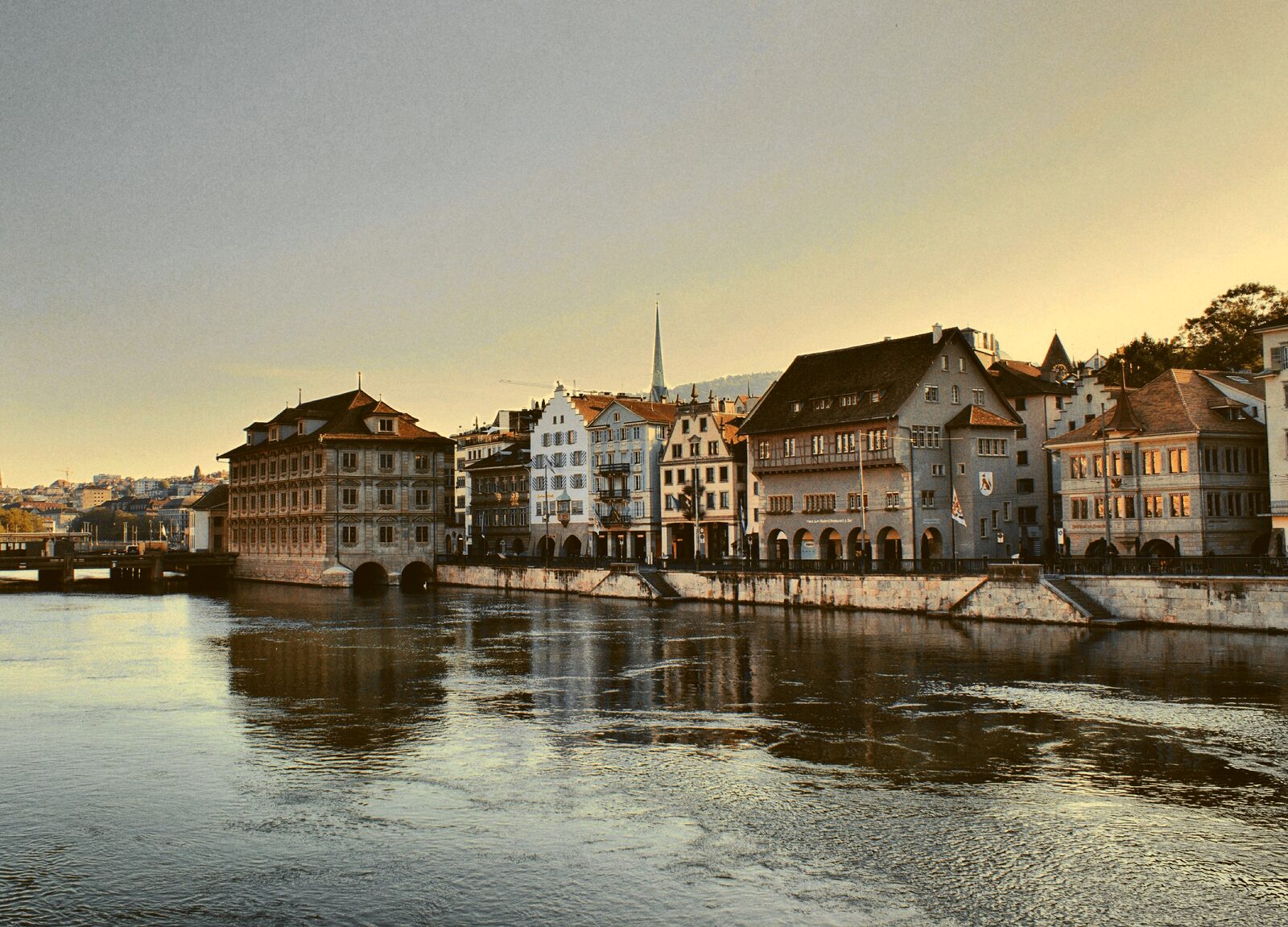 A row of riverside buildings reflected in calm water at dusk.