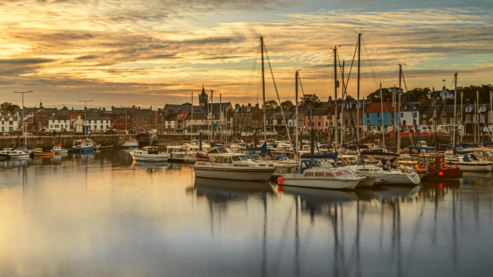 Sailboats moored in a harbor at sunrise with a village on the shore behind.