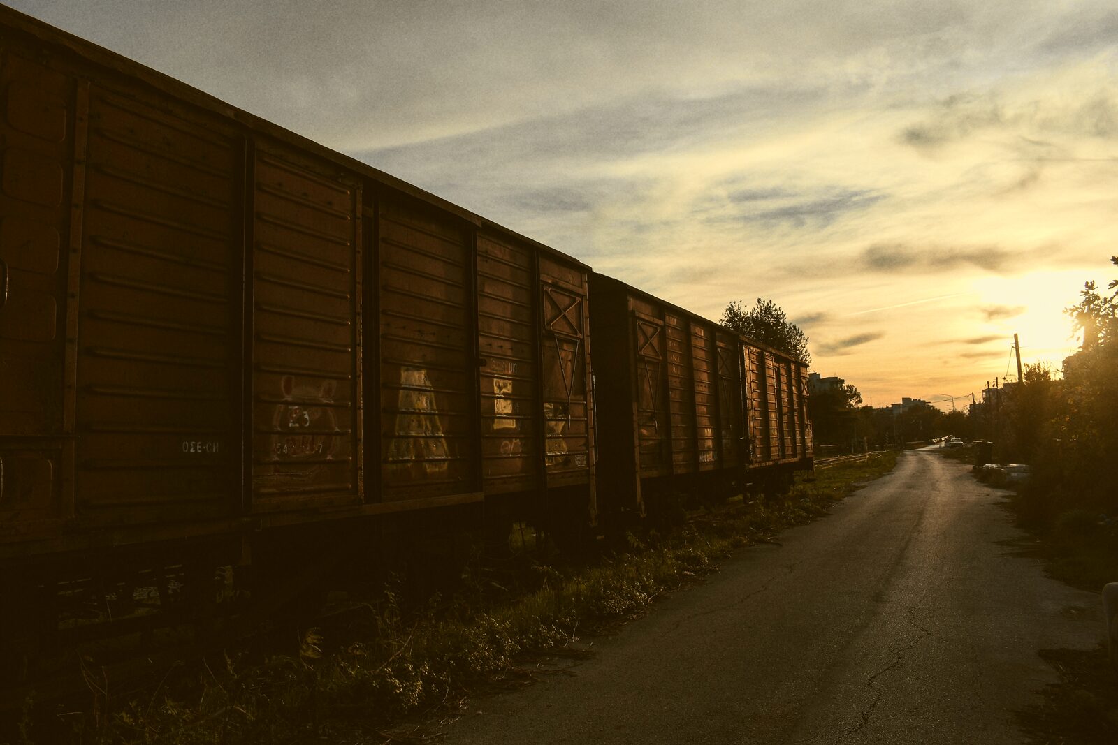 A line of weathered freight boxcars along a track at dusk.