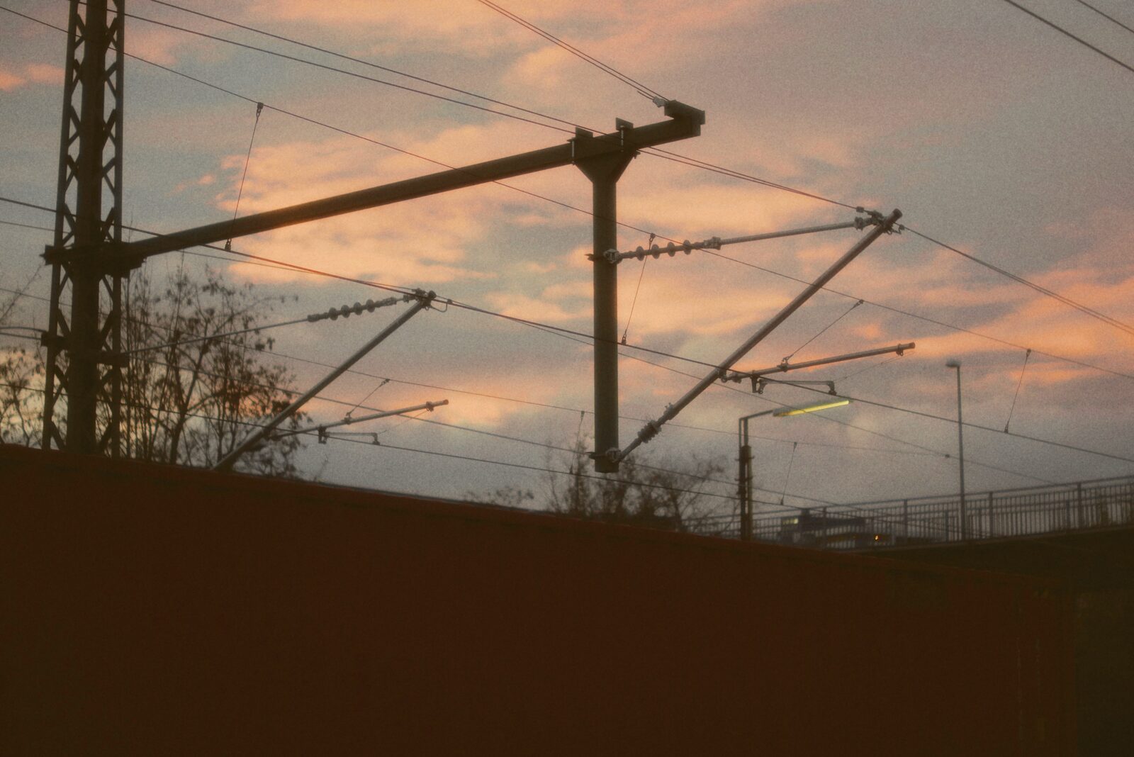 An overhead electric rail line silhouetted against a pink evening sky.
