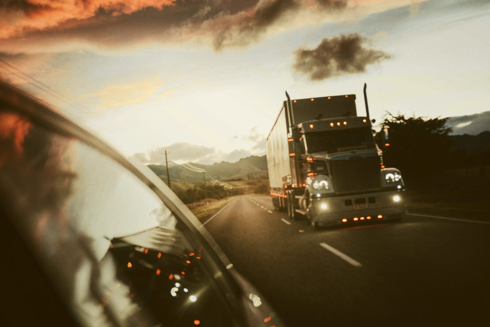 A semi truck driving on a highway at dusk, seen through a car windshield.