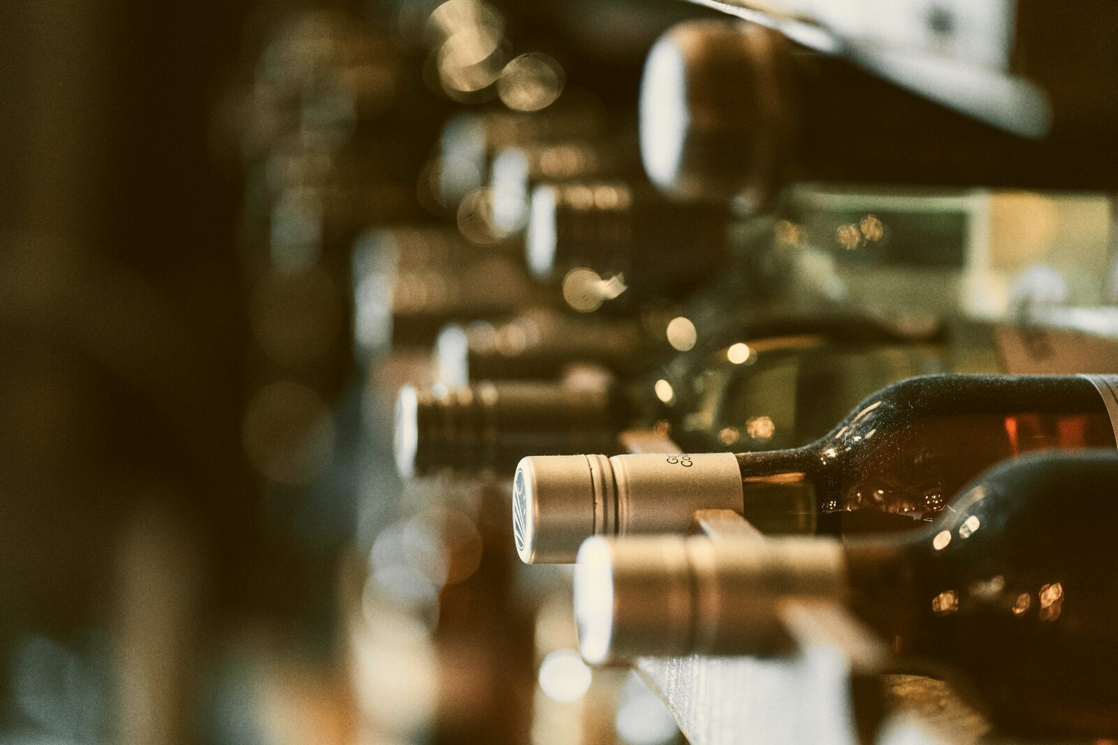 Close-up of wine bottle necks and capsules on a rack, softly lit.