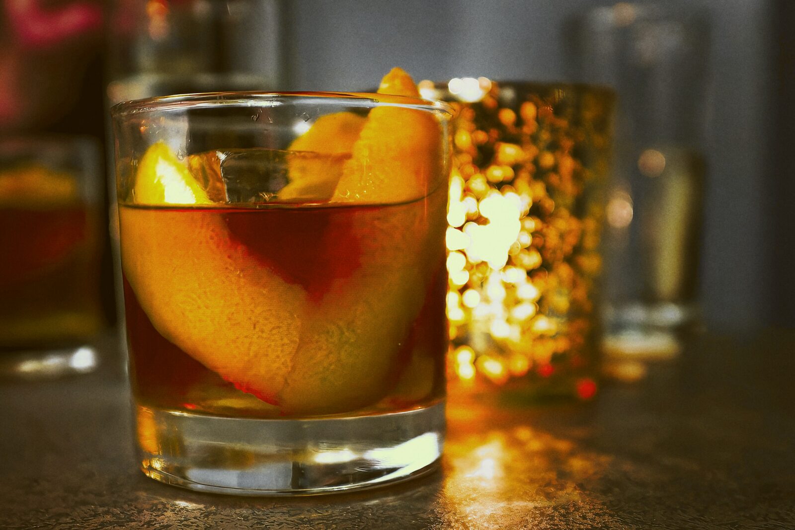 A close-up of an old fashioned cocktail with an orange twist on a bar